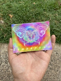 a hand holding a colorful sticker with a butterfly on it