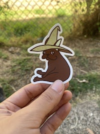 a person holding up a sticker with a brown mule in a hat