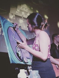 a woman is painting on a canvas in front of a large screen