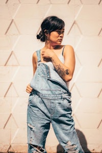 a woman in denim overalls posing in front of a white wall